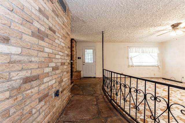 hallway with brick wall, dark tile patterned floors, and a healthy amount of sunlight