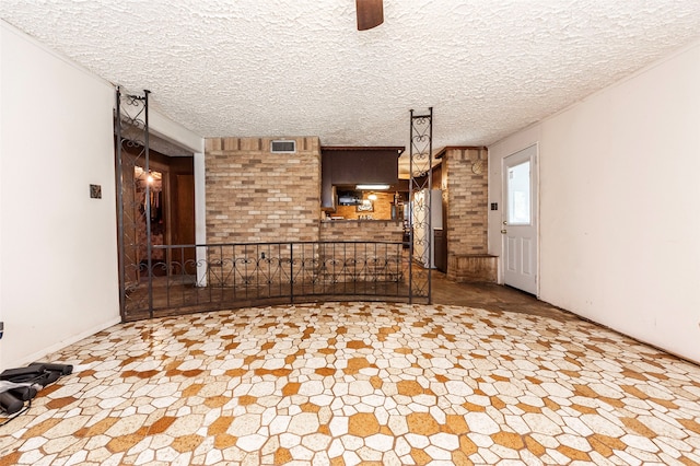 unfurnished living room featuring brick wall, a textured ceiling, and tile patterned flooring