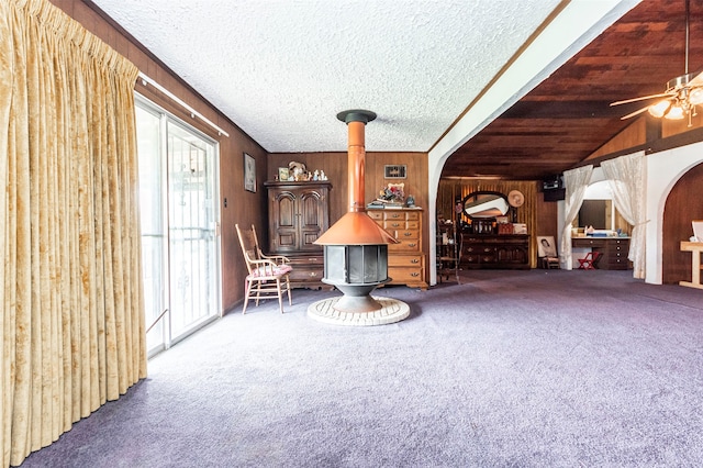 unfurnished living room with carpet flooring, lofted ceiling, wooden walls, a textured ceiling, and ceiling fan