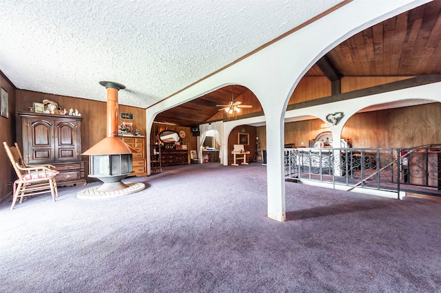 unfurnished living room featuring lofted ceiling, wooden walls, ceiling fan, wooden ceiling, and carpet