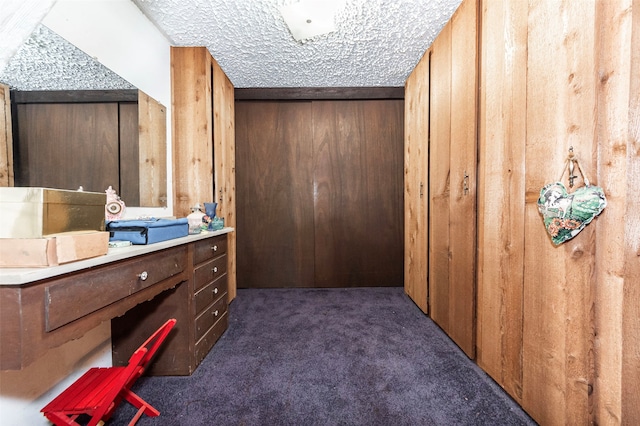 interior space with a textured ceiling, wooden walls, and dark carpet