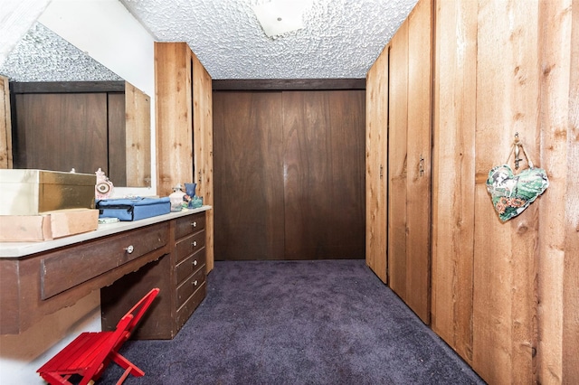 interior space featuring wooden walls, a textured ceiling, and dark colored carpet