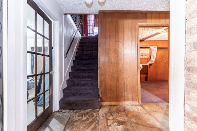 stairs with wood walls, a wealth of natural light, carpet floors, and a textured ceiling