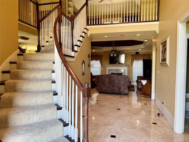 staircase with ceiling fan, a fireplace, a towering ceiling, and light tile floors