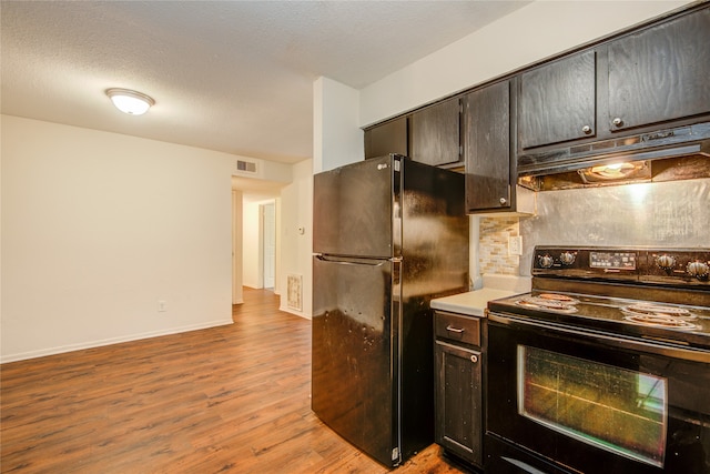 kitchen featuring range with electric stovetop, black fridge, dark brown cabinetry, light wood-type flooring, and backsplash