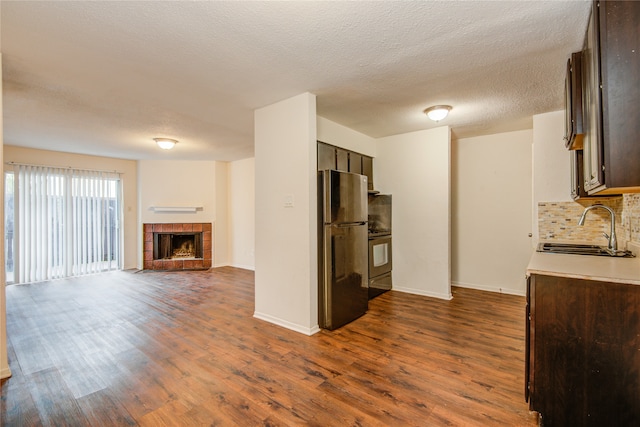 kitchen featuring dark hardwood / wood-style flooring, a tile fireplace, tasteful backsplash, stainless steel fridge, and sink