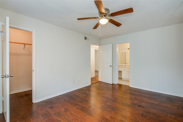 unfurnished bedroom featuring a closet, a spacious closet, dark hardwood / wood-style floors, and ceiling fan