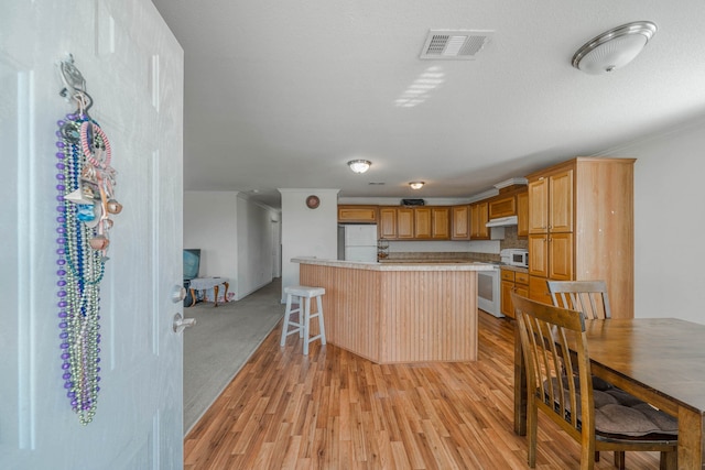 kitchen with a breakfast bar area, white appliances, and light colored carpet