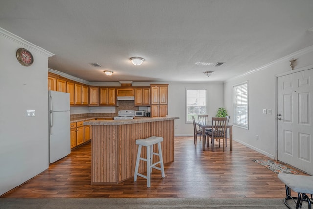 kitchen featuring a center island, a breakfast bar, white appliances, crown molding, and dark hardwood / wood-style floors