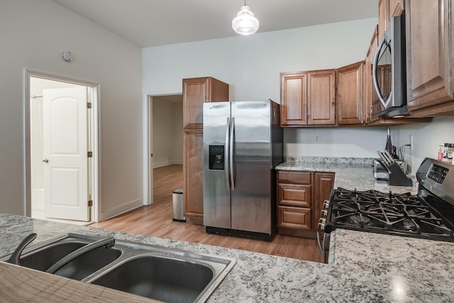 kitchen with brown cabinetry, light wood-style flooring, stainless steel appliances, and a sink