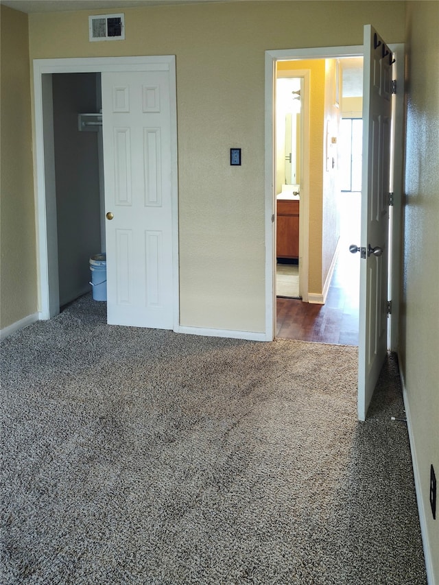 unfurnished bedroom with a closet, dark carpet, and ensuite bathroom