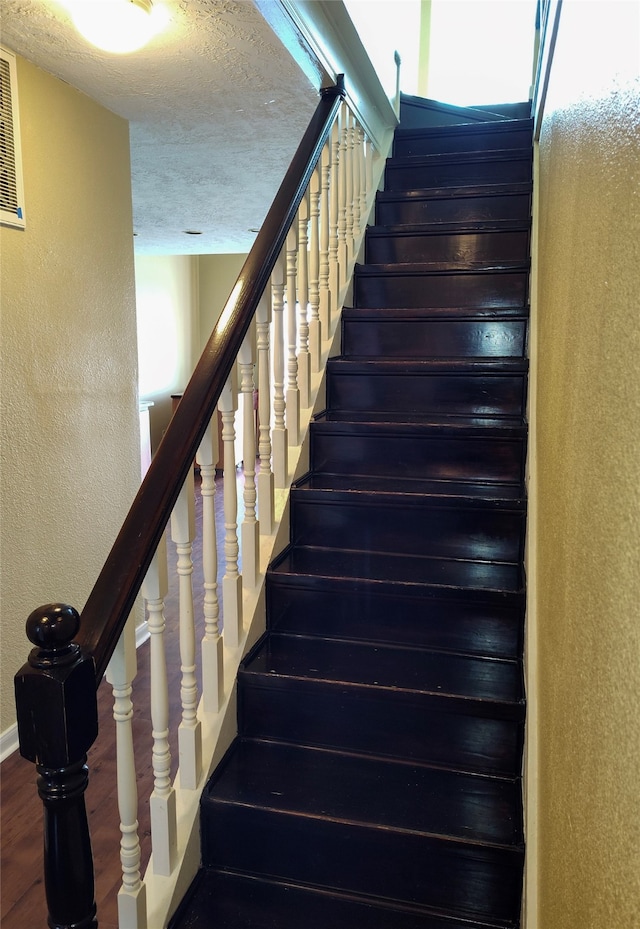 stairs with a textured ceiling and dark wood-type flooring