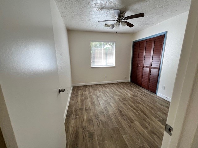 unfurnished bedroom featuring a textured ceiling, a closet, ceiling fan, and dark wood-type flooring