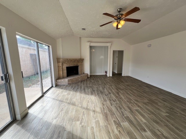 unfurnished living room featuring hardwood / wood-style flooring, a brick fireplace, vaulted ceiling, ceiling fan, and a textured ceiling