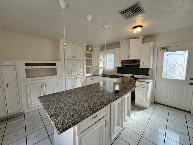 kitchen with light tile floors, a kitchen island, backsplash, and white cabinetry