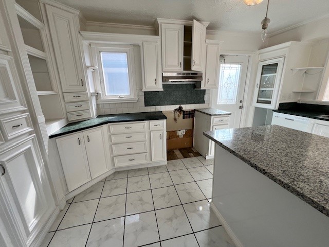 kitchen featuring light tile floors, dark stone counters, crown molding, white cabinets, and backsplash