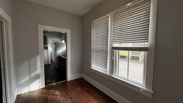 unfurnished bedroom with stainless steel fridge and dark hardwood / wood-style flooring