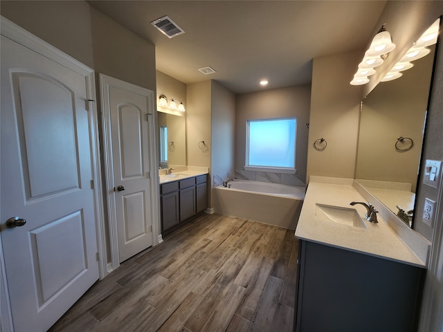 bathroom with dual bowl vanity, a bath to relax in, and wood-type flooring