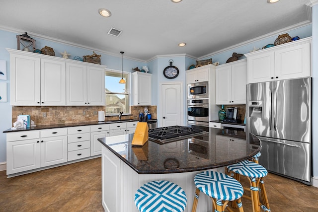 kitchen featuring appliances with stainless steel finishes, white cabinetry, backsplash, a kitchen bar, and a center island