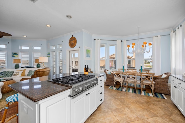 kitchen featuring white cabinetry, hanging light fixtures, a center island, dark stone counters, and stainless steel gas stovetop