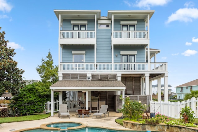 back of property featuring a swimming pool with hot tub, a patio, a balcony, and a fire pit