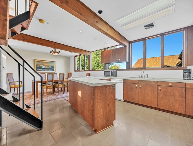 kitchen with white dishwasher, a kitchen island, light tile floors, beam ceiling, and an inviting chandelier