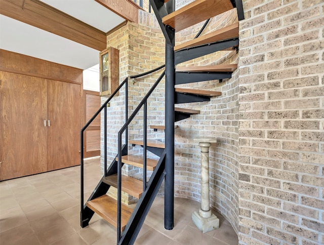 stairs featuring light tile flooring and brick wall