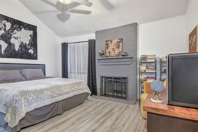 bedroom featuring brick wall, a brick fireplace, ceiling fan, light hardwood / wood-style floors, and vaulted ceiling