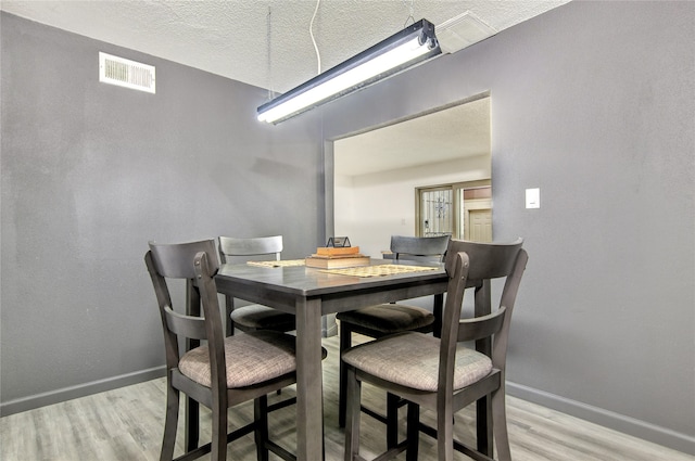 dining space with a textured ceiling and light hardwood / wood-style flooring