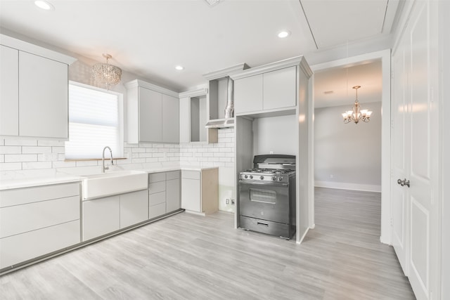 kitchen with light hardwood / wood-style floors, a chandelier, black range with gas stovetop, sink, and backsplash