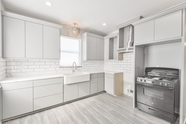 kitchen with an inviting chandelier, light wood-type flooring, black range with gas cooktop, sink, and decorative backsplash