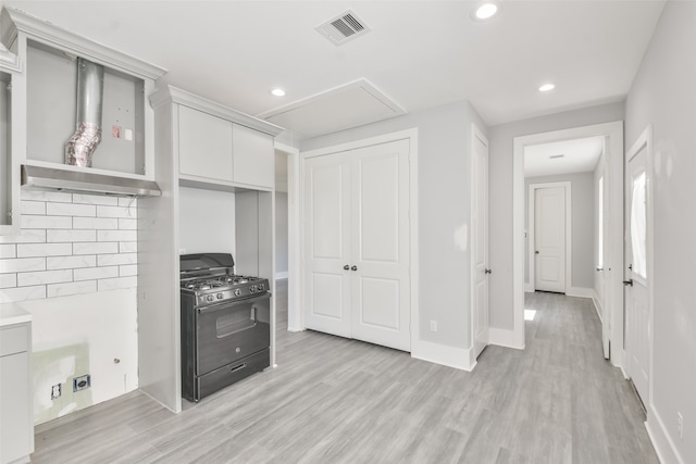 kitchen featuring decorative backsplash, light wood-type flooring, black gas range oven, and white cabinetry