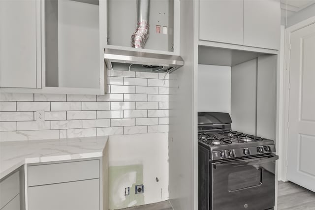 kitchen featuring black gas stove, light wood-type flooring, exhaust hood, light stone countertops, and decorative backsplash