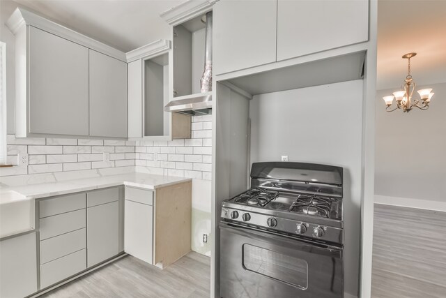 kitchen with light hardwood / wood-style floors, a chandelier, gray cabinetry, gas range, and decorative backsplash