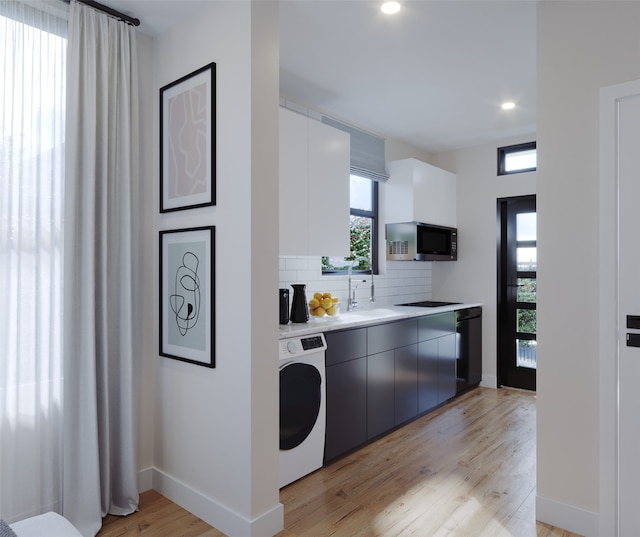 kitchen featuring light hardwood / wood-style floors, washer / dryer, black appliances, and a healthy amount of sunlight