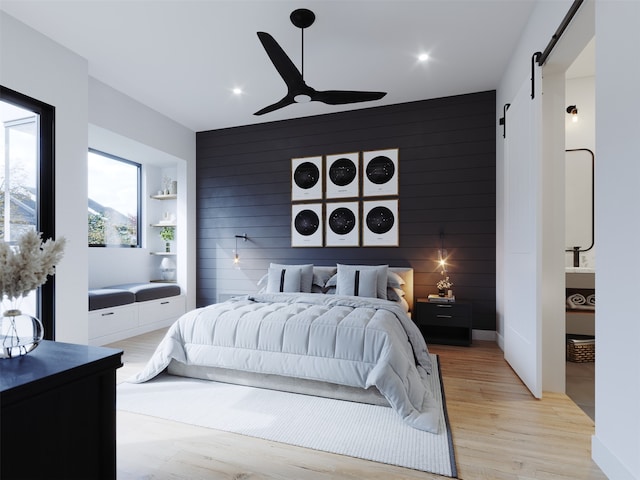 bedroom with ceiling fan, wooden walls, a barn door, and light hardwood / wood-style floors