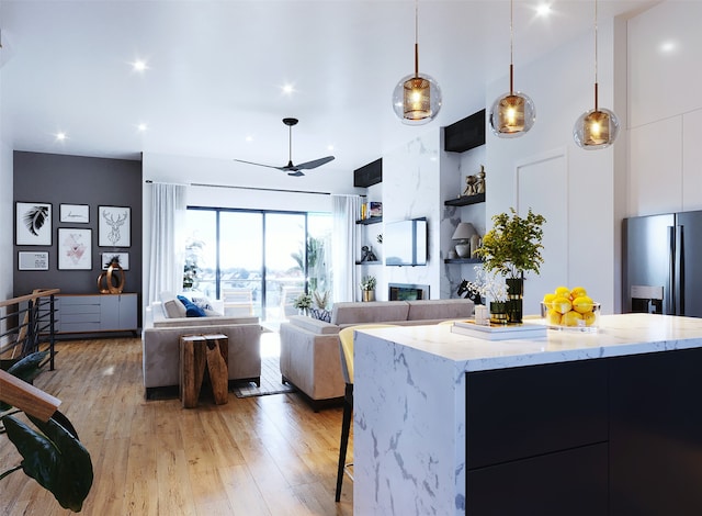 kitchen with a kitchen island, pendant lighting, light wood-type flooring, light stone countertops, and ceiling fan