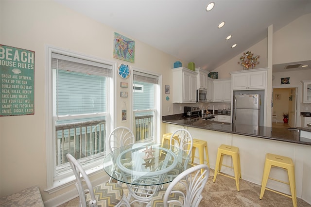 kitchen featuring a breakfast bar, backsplash, white cabinetry, lofted ceiling, and stainless steel appliances