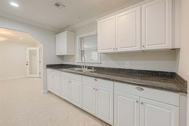 kitchen with dark stone countertops, light tile patterned floors, ornamental molding, sink, and white cabinetry