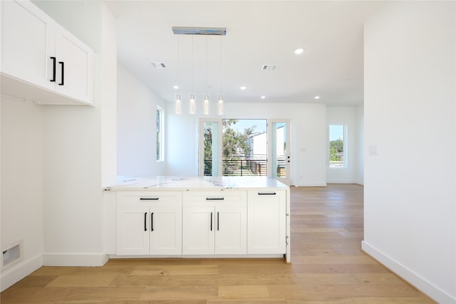 kitchen with light stone counters, kitchen peninsula, hanging light fixtures, white cabinetry, and light hardwood / wood-style flooring