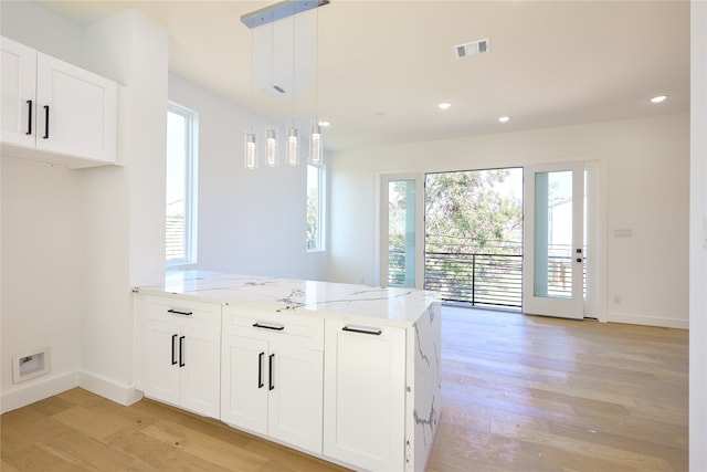 kitchen featuring light hardwood / wood-style flooring, hanging light fixtures, light stone counters, and white cabinetry