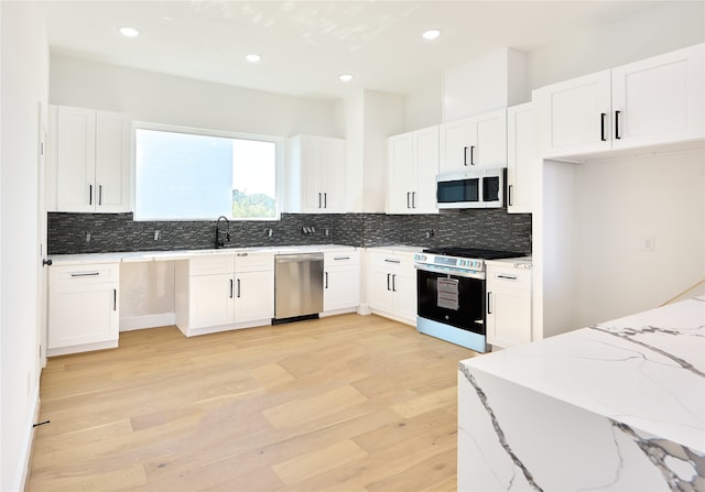 kitchen featuring white cabinets, tasteful backsplash, light hardwood / wood-style flooring, stainless steel appliances, and light stone countertops