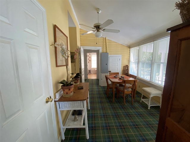 dining room featuring wood walls, ceiling fan, and vaulted ceiling