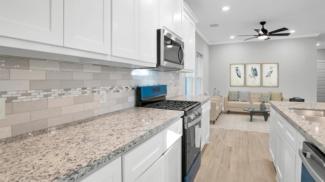 kitchen featuring ornamental molding, appliances with stainless steel finishes, light hardwood / wood-style floors, light stone counters, and white cabinetry