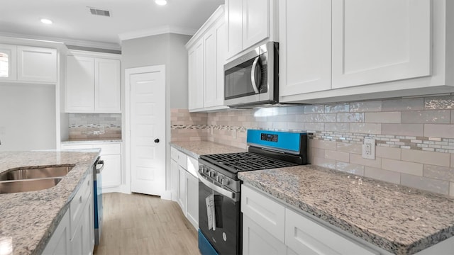 kitchen featuring appliances with stainless steel finishes, tasteful backsplash, ornamental molding, light hardwood / wood-style floors, and white cabinetry