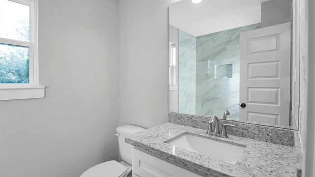 bathroom featuring a tile shower, vanity, and toilet