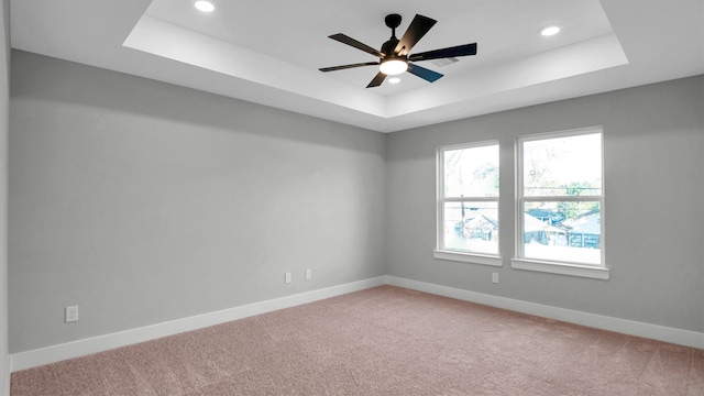 carpeted empty room with a raised ceiling and ceiling fan