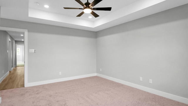 carpeted spare room with ceiling fan and a tray ceiling