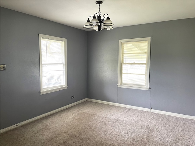 spare room with a wealth of natural light, a chandelier, and carpet floors