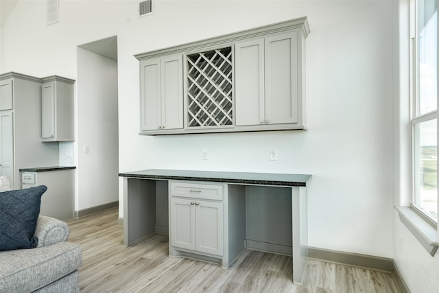 bar featuring gray cabinetry, light hardwood / wood-style floors, and dark stone counters